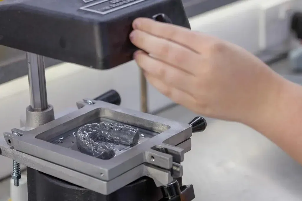 A vacuum-forming station pulling Essix stock over a printed arch model