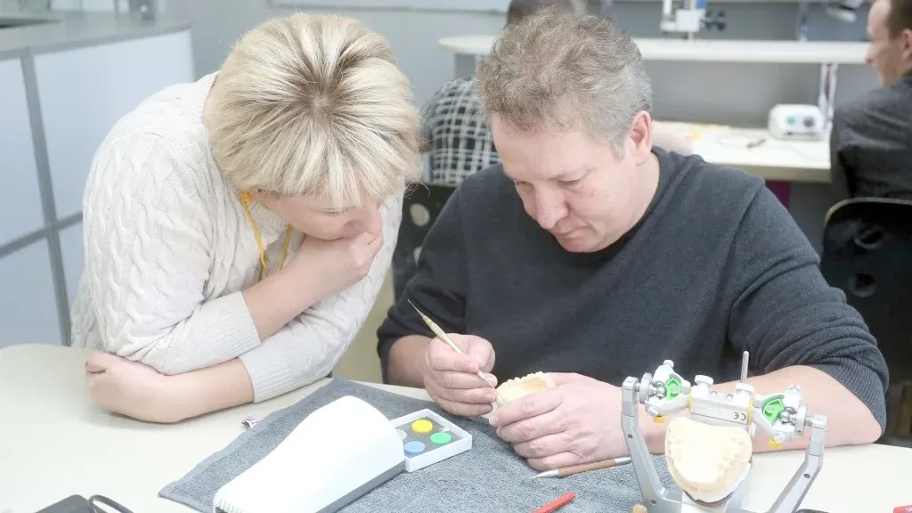 Ceramist refining surface stain and glaze on an anterior crown under bench lighting